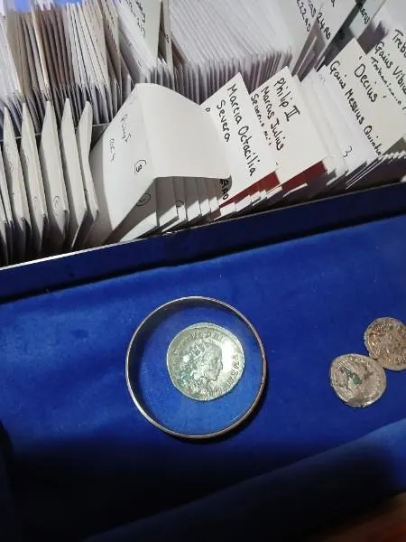 Catalogued coins of the Weobley Hoard in labelled envelopes naming Roman emperors, with a denarius displayed on blue velvet